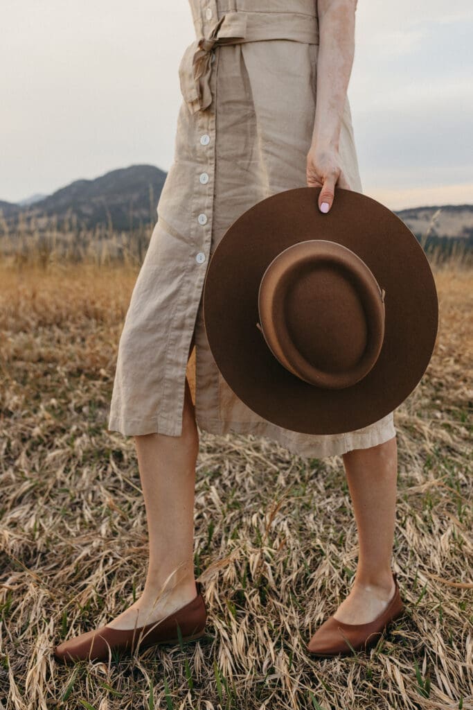 woman walking through grass holding hat